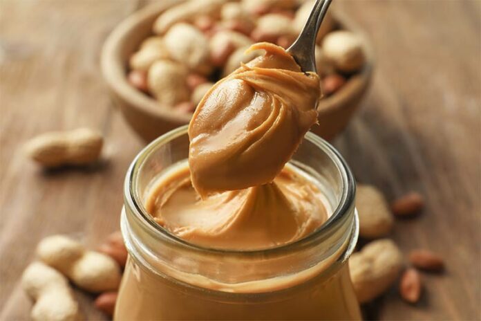 Spoon dipping into a large jar of peanut butter for cooking