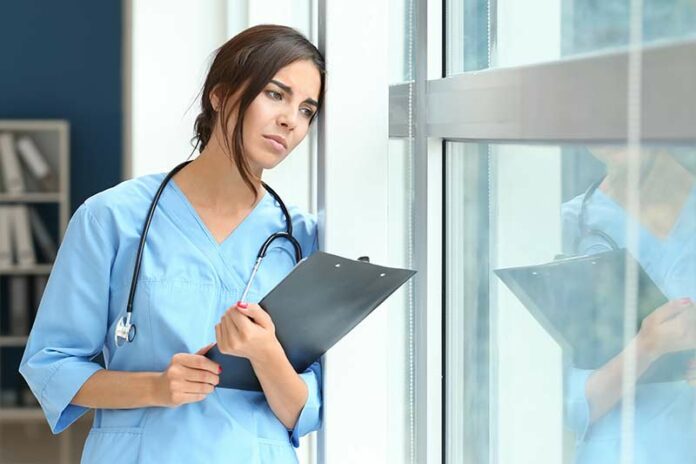 Female nurse in blue scrubs upset with bickering and backstabbing in the workplace