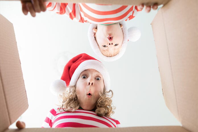 Two kids with Christmas gear on looking into an open box together