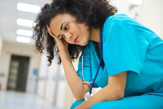 Depressed female African American nurse in blue scrubs sitting